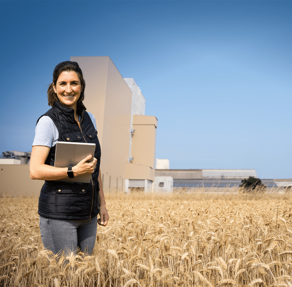 Une femme dans un champ de blé devant une usine d'aliment