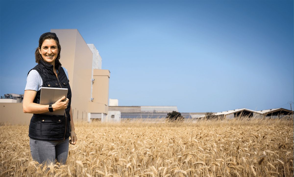 Une femme dans un champ de blé devant une usine d'aliment