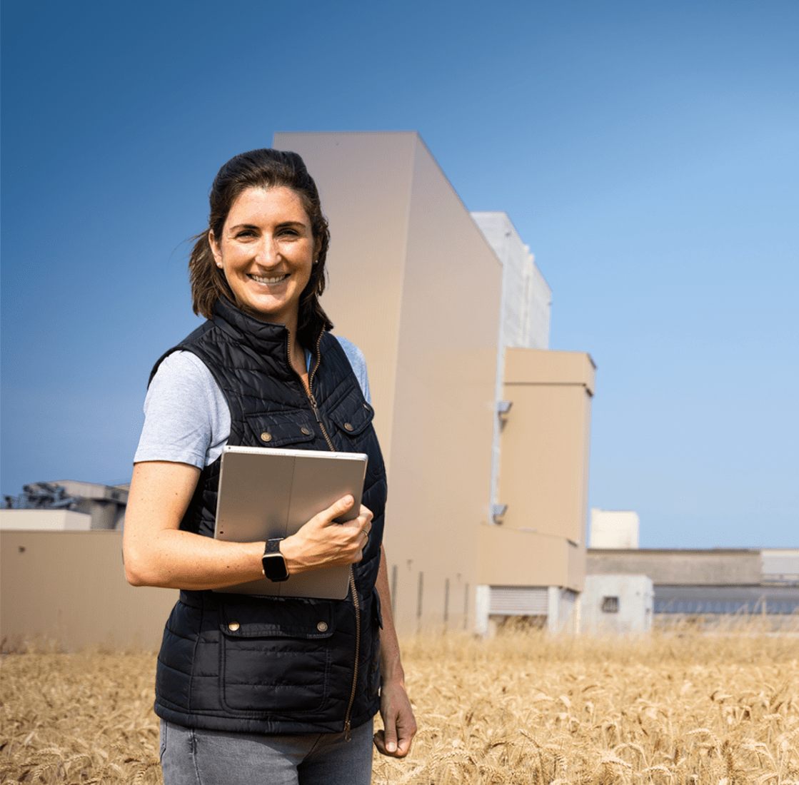 Une femme dans un champ de blé devant une usine d'aliment