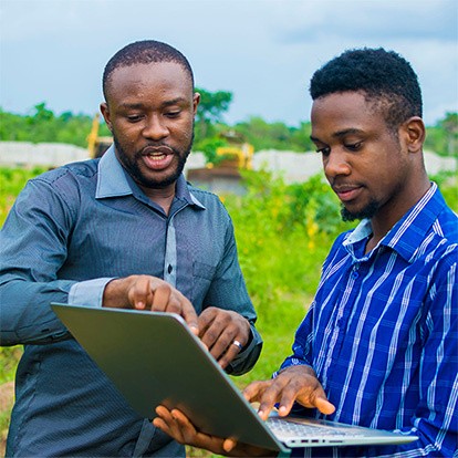 Deux Ivoiriens devant un ordinateur portable dans un champs